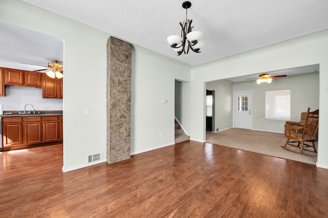 unfurnished living room featuring wood finished floors, stairs, and ceiling fan with notable chandelier