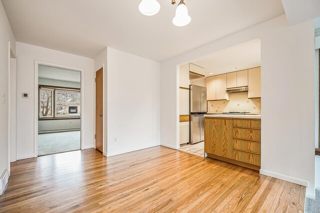 kitchen featuring under cabinet range hood, light wood finished floors, light countertops, and freestanding refrigerator