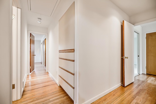 hall with attic access, light wood-type flooring, and baseboards