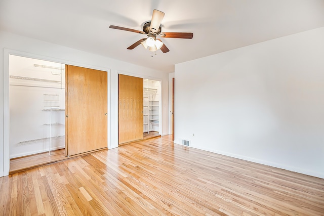 unfurnished bedroom featuring light wood-style flooring, a ceiling fan, visible vents, and two closets