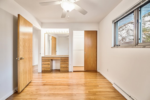 unfurnished bedroom featuring built in desk, light wood finished floors, baseboards, baseboard heating, and ceiling fan