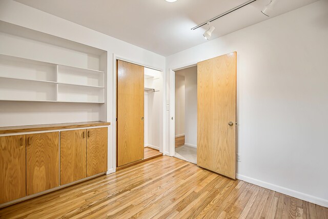 empty room with light wood-type flooring, baseboards, and track lighting