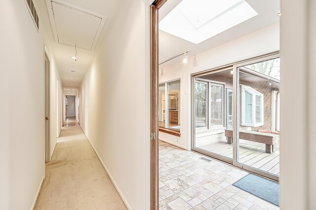 corridor with visible vents, baseboards, attic access, light carpet, and rail lighting