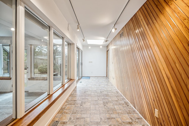 corridor with visible vents, wood walls, rail lighting, and stone finish floor