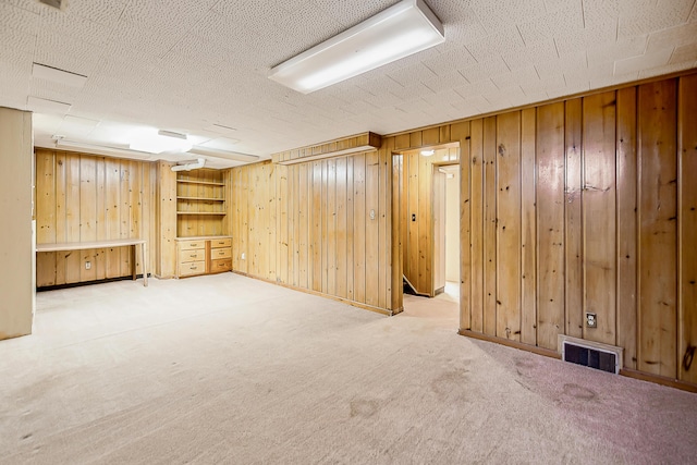 finished below grade area featuring visible vents, carpet flooring, a textured ceiling, and wood walls