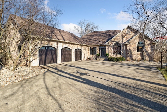 french country inspired facade with stone siding, driveway, a shingled roof, and a garage