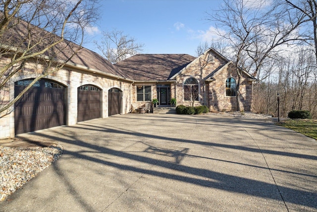 french provincial home featuring an attached garage, stone siding, driveway, and a shingled roof