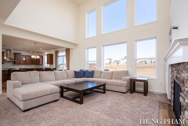 carpeted living room with a high ceiling, a fireplace, baseboards, and a chandelier