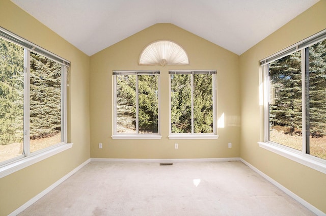 empty room with a wealth of natural light, visible vents, light colored carpet, and vaulted ceiling