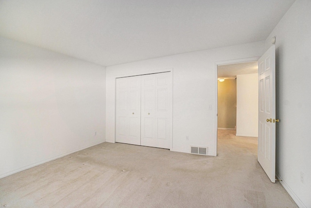 unfurnished bedroom with a closet, visible vents, light colored carpet, and baseboards