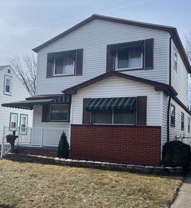 view of front of house featuring a front lawn, covered porch, and brick siding