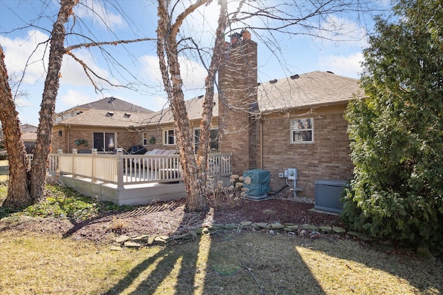 back of house featuring brick siding, a chimney, a deck, and a shingled roof