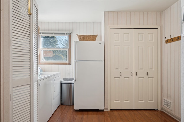 laundry room featuring visible vents, wood finished floors, wooden walls, laundry area, and washing machine and clothes dryer