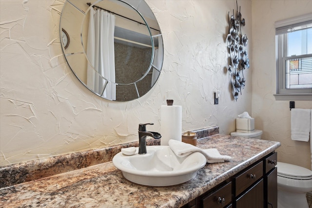 bathroom with vanity, toilet, and a textured wall