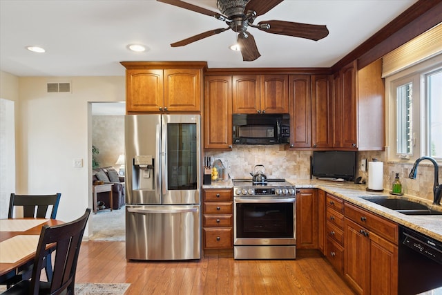 kitchen with visible vents, a sink, decorative backsplash, black appliances, and light wood-style floors