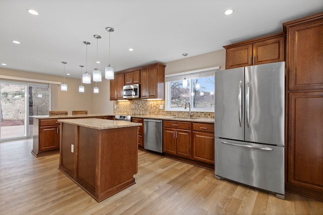 kitchen featuring a kitchen island, light wood-type flooring, brown cabinets, stainless steel appliances, and a sink