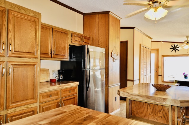 kitchen with ornamental molding, a ceiling fan, wood counters, freestanding refrigerator, and brown cabinetry