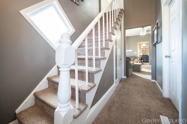 stairs with visible vents, baseboards, ceiling fan, carpet flooring, and a high ceiling