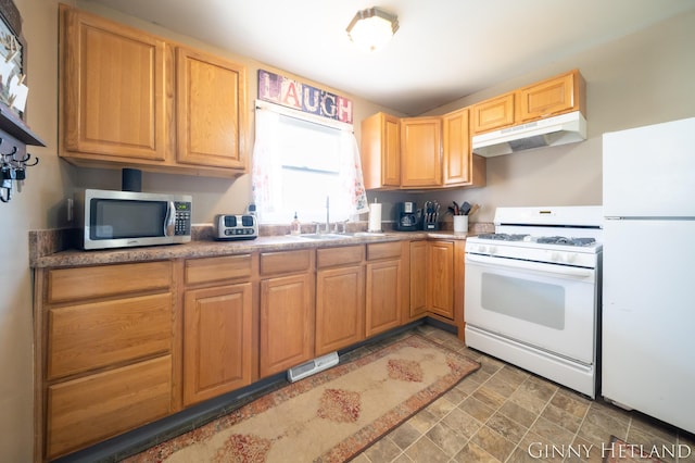 kitchen featuring under cabinet range hood, stone finish floor, white appliances, and a sink