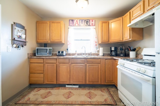 kitchen featuring stainless steel microwave, under cabinet range hood, light tile patterned floors, white range with gas cooktop, and a sink