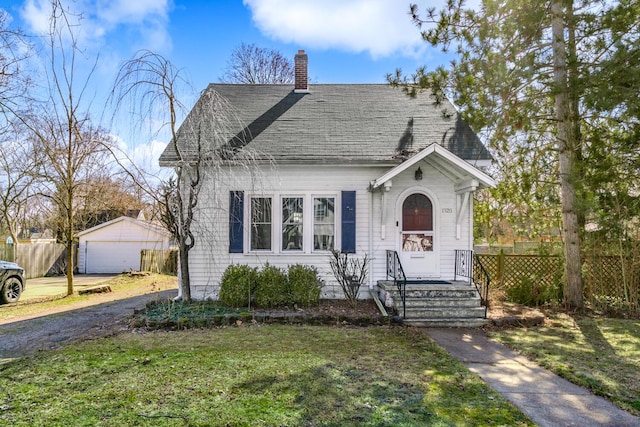 bungalow-style house with a shingled roof, fence, a front yard, a chimney, and an outbuilding