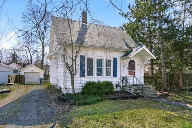 view of front of property with a detached garage, a front yard, a chimney, an outdoor structure, and driveway