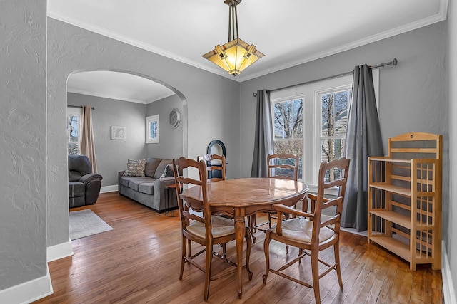 dining room with ornamental molding, arched walkways, wood-type flooring, baseboards, and a textured wall