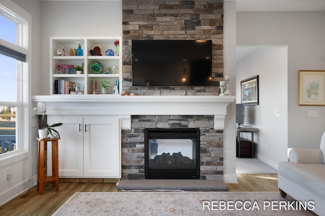 living room featuring a stone fireplace, baseboards, and wood finished floors