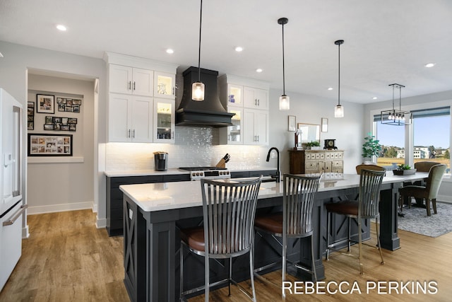 kitchen with premium range hood, a kitchen island with sink, range with gas stovetop, high end white fridge, and white cabinets