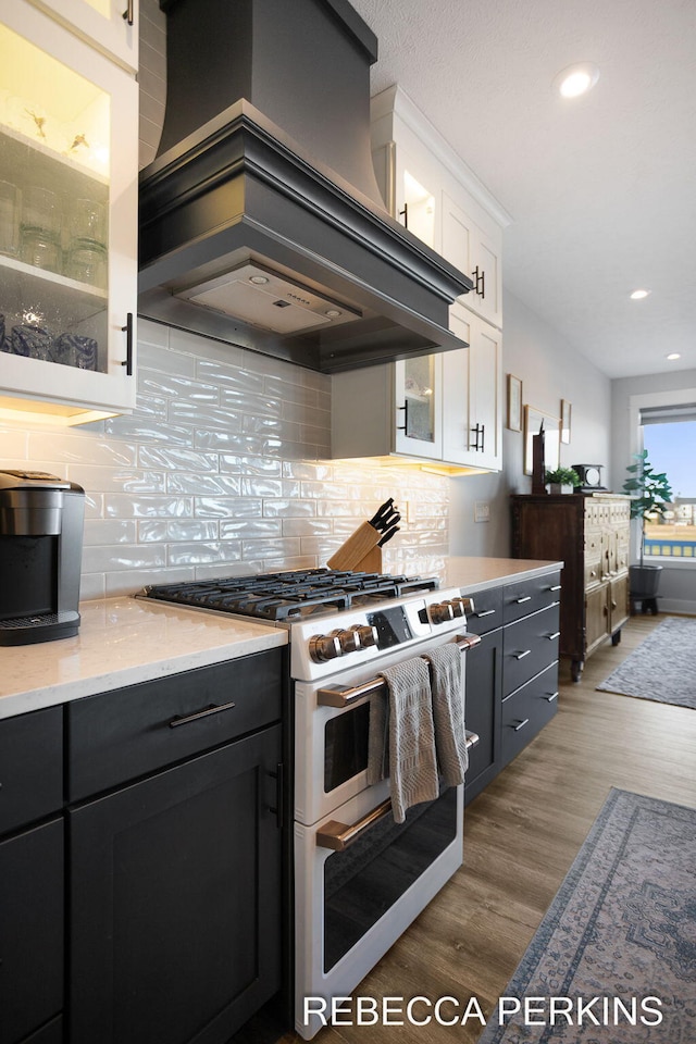 kitchen featuring wood finished floors, range with two ovens, decorative backsplash, white cabinetry, and wall chimney range hood