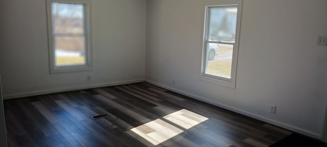 unfurnished room featuring dark wood finished floors, visible vents, and baseboards