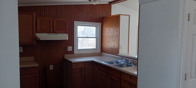 kitchen featuring light countertops, brown cabinetry, under cabinet range hood, and a sink