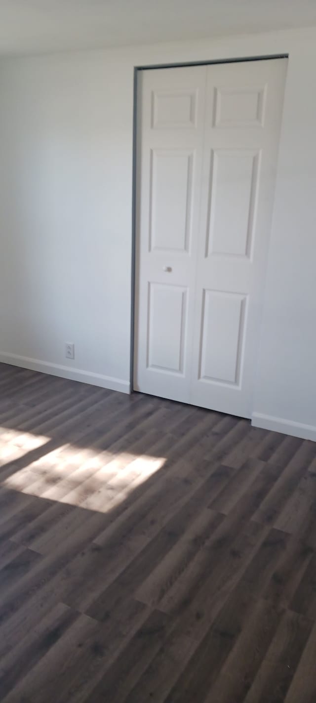 unfurnished bedroom featuring a closet, dark wood-type flooring, and baseboards