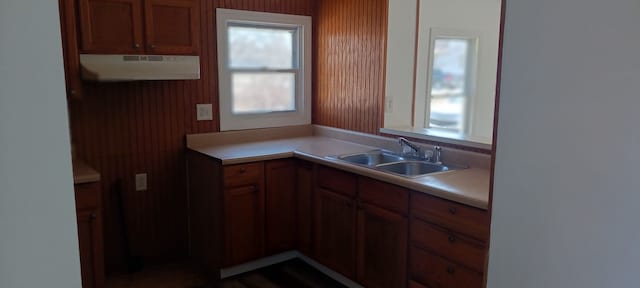 kitchen with light countertops, brown cabinetry, under cabinet range hood, and a sink