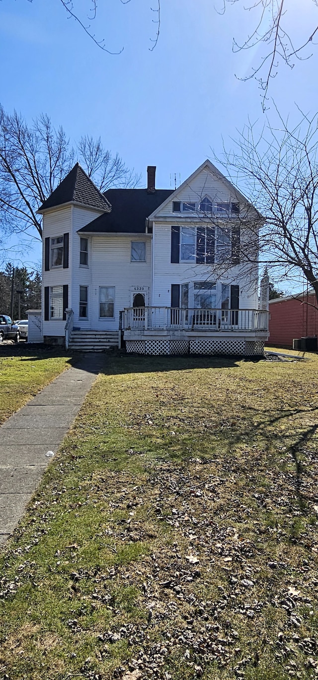 view of front facade with a wooden deck, a chimney, and a front lawn