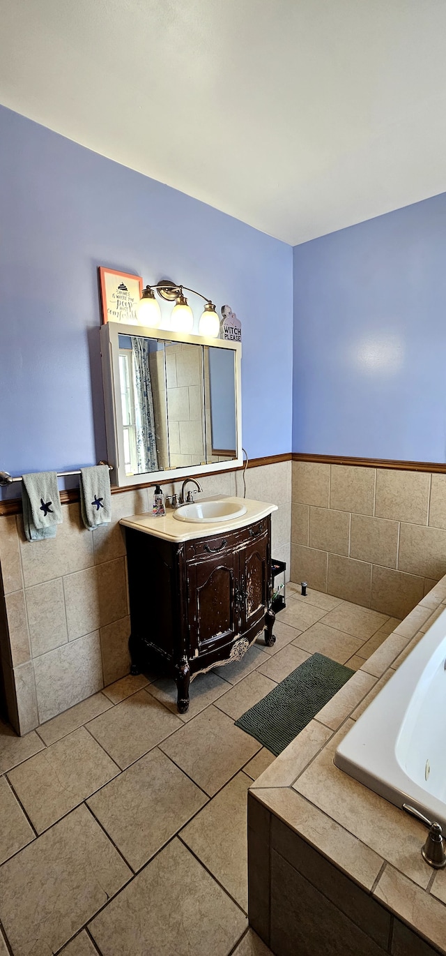 bathroom with vanity, a tub with jets, wainscoting, tile walls, and tile patterned floors