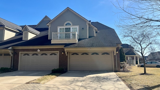 view of front of property with a balcony, brick siding, driveway, and roof with shingles