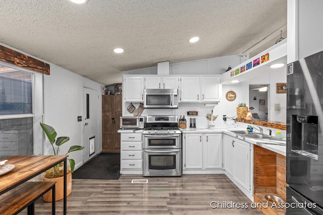 kitchen featuring vaulted ceiling, appliances with stainless steel finishes, wood finished floors, white cabinets, and a sink