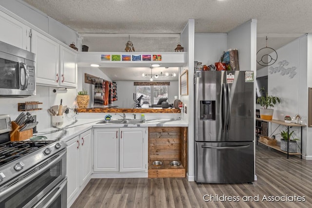 kitchen with a sink, appliances with stainless steel finishes, wood finished floors, and white cabinetry