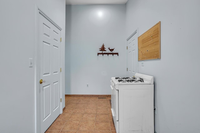 kitchen with white gas stove, light tile patterned floors, and baseboards