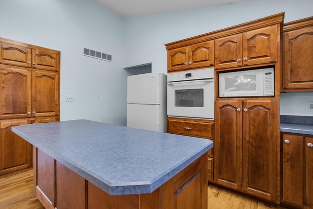 kitchen featuring white appliances, brown cabinetry, visible vents, light wood finished floors, and a kitchen island