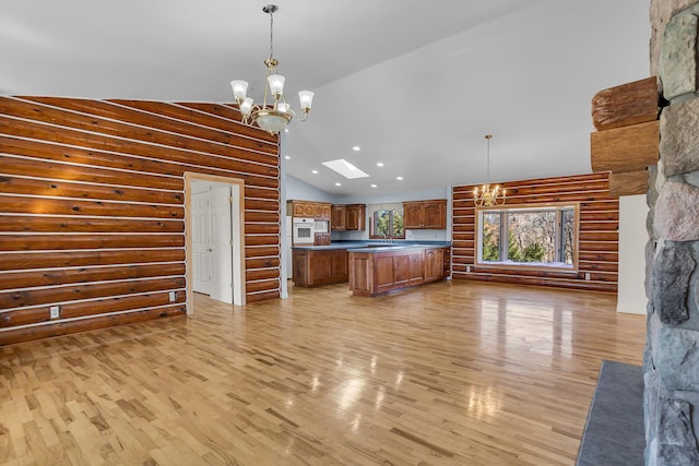 kitchen with open floor plan, light wood-type flooring, an inviting chandelier, brown cabinetry, and high vaulted ceiling