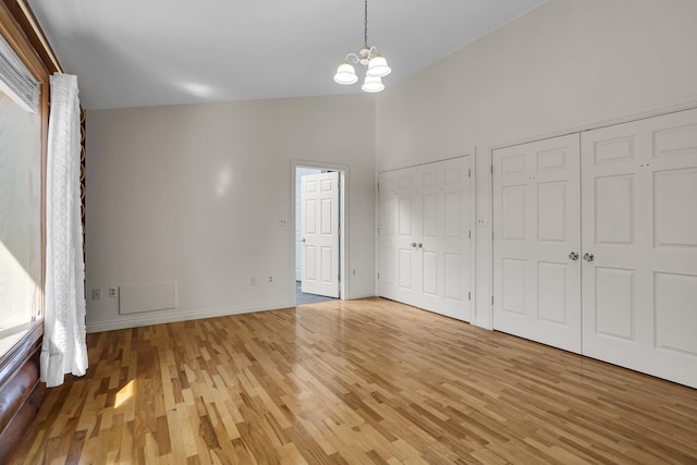 unfurnished bedroom featuring light wood-style floors, baseboards, two closets, and a chandelier