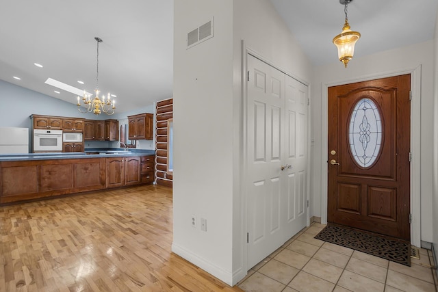 foyer entrance with visible vents, light wood finished floors, an inviting chandelier, and vaulted ceiling