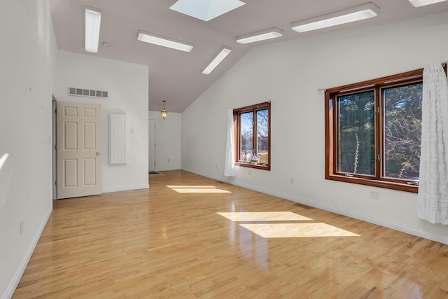 empty room with visible vents, light wood-style flooring, baseboards, and vaulted ceiling