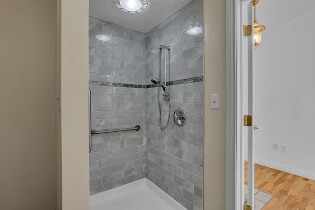 bathroom with wood finished floors, baseboards, and tiled shower