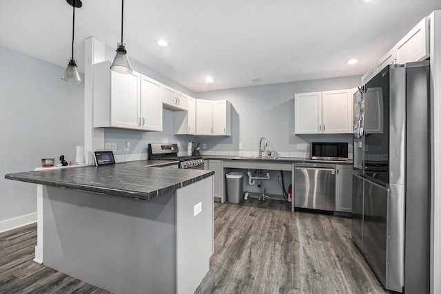 kitchen featuring dark countertops, dark wood-type flooring, appliances with stainless steel finishes, a peninsula, and a sink