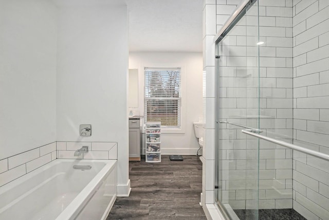full bathroom with toilet, wood finished floors, baseboards, a stall shower, and a garden tub