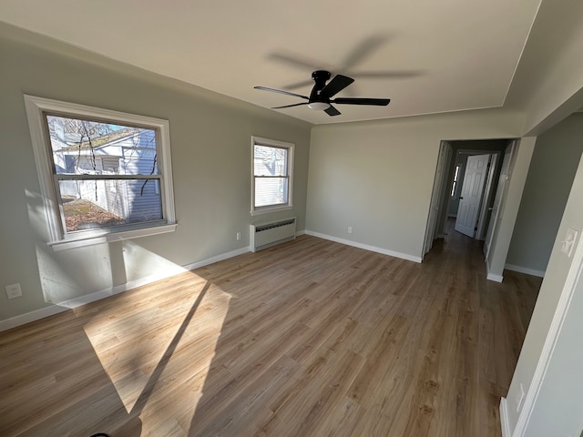 empty room featuring baseboards, radiator heating unit, and light wood finished floors