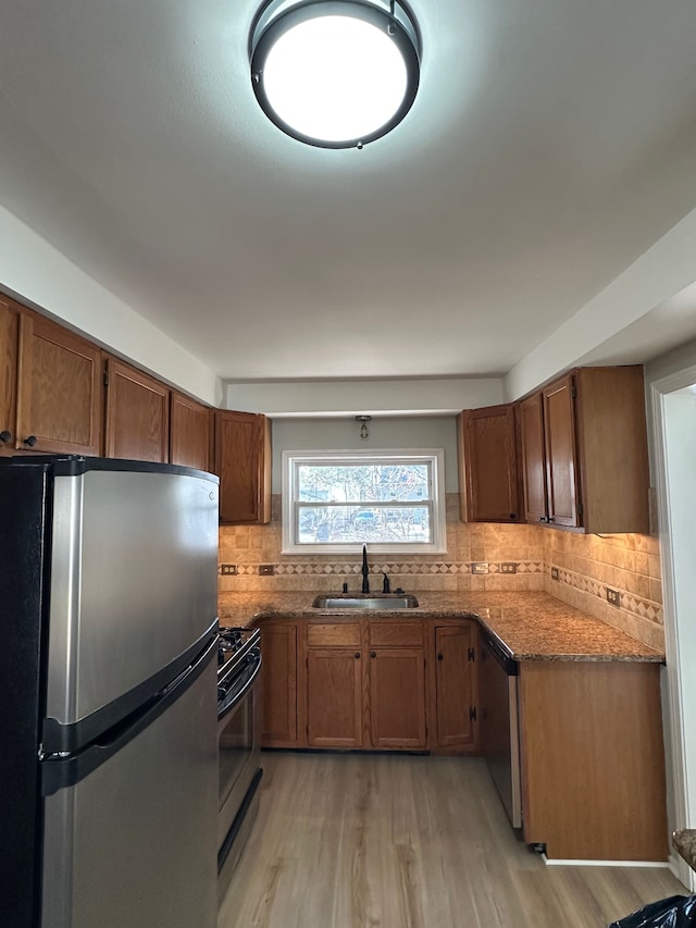 kitchen featuring light wood finished floors, dark stone counters, a sink, stainless steel appliances, and tasteful backsplash